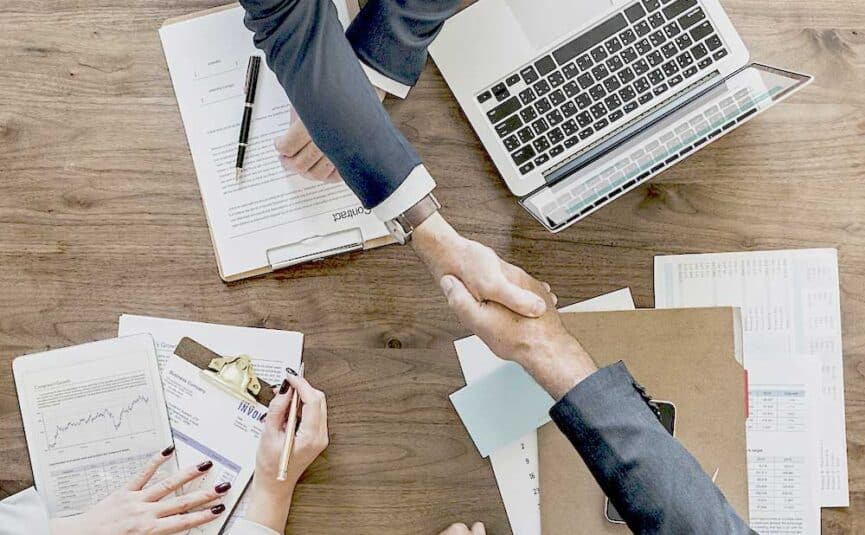 Two people shaking hands over a laptop while discussing the definition of insurance premium funding.