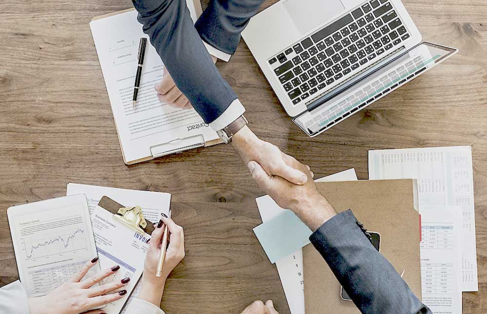 Two people shaking hands over a laptop while discussing the definition of insurance premium funding.